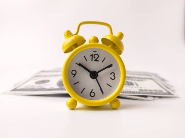 Küçük, sarı, klasik bir analog çalar saat. Bir yığın Amerikan dolarının önünde duruyor..