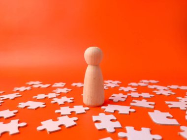 Tahta tahta bebek turuncu arka planda beyaz yapboz parçaları ile çevrili..