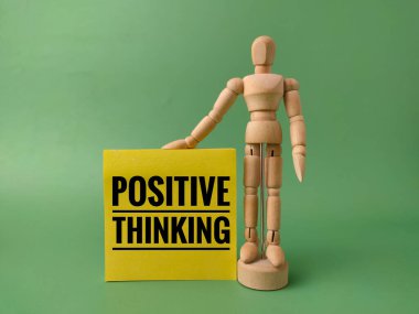 Yeşil arka planda ahşap figürle sarı nota yazılmış olumlu bir düşünce..