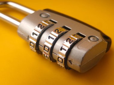 Resimde gösterilen nesne sarı arkaplanda küçük bir asma kilit kombinasyonu..