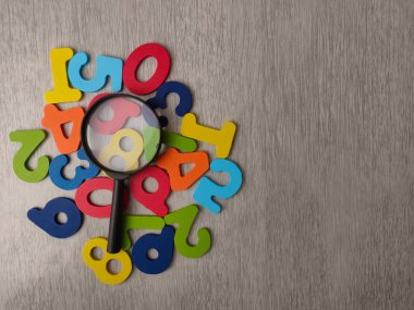 Resim, öğrenmeyi ve keşfi sembolize eden renkli ahşap harflerin üzerine büyüteç koyuyor..