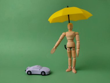 Oyuncak arabanın üzerinde sarı bir şemsiye tutan ahşap figür bir sigorta acentesini ya da güvenlik sigortasını simgeliyor..