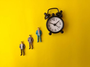 İş adamlarının minyatür figürleri sarı arka planda alarm çalar..