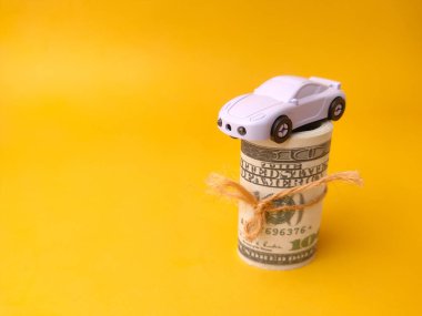 Oyuncak araba, araç sahibi olmakla ilgili kavramları sembolize ederek bir rulo Amerikan doları banknotunun üzerinde dinleniyor..
