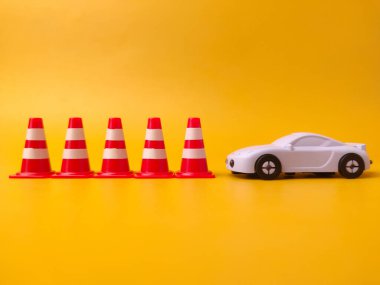 Minyatür trafik konileri, sarı arka planda oyuncak bir arabanın yanında..