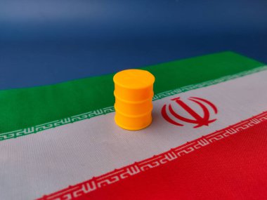 Resimde İran bayrağının tepesine küçük sarı bir plastik varil veya yağ varili konuyor..