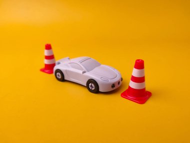 Oyuncak spor araba sarı bir yüzey üzerinde üç minyatür kırmızı ve beyaz trafik konisinin yanına yerleştirildi..
