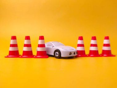 Görüntüde, genellikle yol sahnelerini canlandırmak amacıyla eğitim amaçlı kullanılan mor bir oyuncak arabayı çevreleyen minyatür oyuncak trafik konileri yer alıyor..