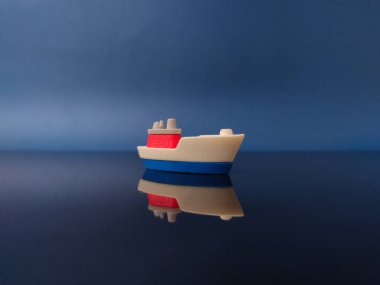 Bu küçük plastik bir oyuncak tekne, muhtemelen koyu mavi arka planda yansıması olan bir kargo gemisi..