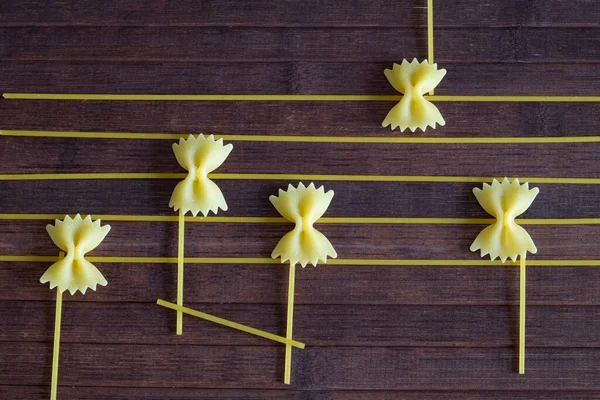 Creative composition of a musical score, the notes are represented by bow tie-shaped paste, the lines of the score with spaghetti, the background is a wooden table.