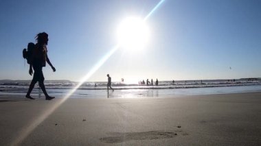 Sahilde kumsalda yürüyen bir adam. Arka planda güneş var.