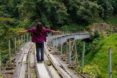 Arkadan gelen rastalı ve kare gömlekli bir adam tren raylarında kolları açık ve gökyüzüne bakıyor.