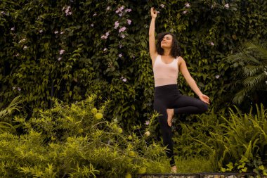 Kıvırcık saçlı kadın yoga pozisyonunda duruyor.