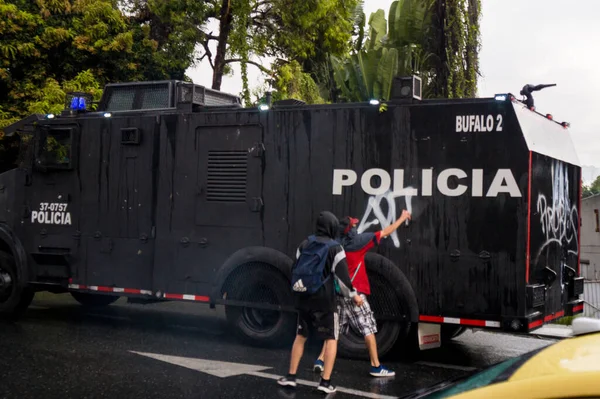MEDELLN, COLOMBIA - 28 Nisan 2021: Gençler diğer protestoculara su püskürtürken zırhlı bir polis aracını çiziyorlar