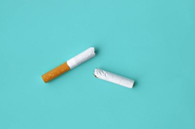 Cigarette broken in half on blue background, concept of giving up smoking