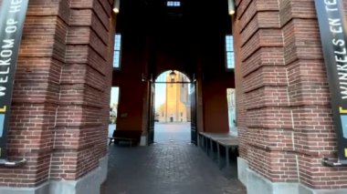 WOERDEN, Hollanda - 25 Mart 2021: Woerden şehir merkezindeki Kerkplein 'e giriş kapısından ateş edin. Meydanda, altın saat boyunca güneş tarafından aydınlatılan Petruskerk manzarası var.. 