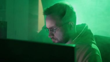 Gözlüklü beyaz bir adam bilgisayarda çalışır, yazar, bilgiyi kontrol eder, kodlar, çalışır, programlar.