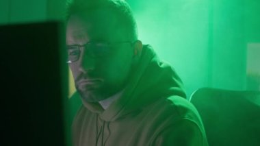 Gözlüklü beyaz bir adam bilgisayarda çalışır, yazar, bilgiyi kontrol eder, kodlar, çalışır, programlar.