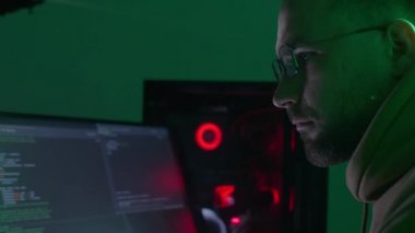 Gözlüklü beyaz bir adam bilgisayarda çalışıyor, kodları giriyor, klavyede çok hızlı yazıyor, bilgiyi kontrol ediyor, kodluyor, çalışıyor, programlıyor.