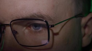 Gözlüklü beyaz bir adam, bilgilerle sıkı çalışır, odaklanır ve dikkatle ekrana bakar.