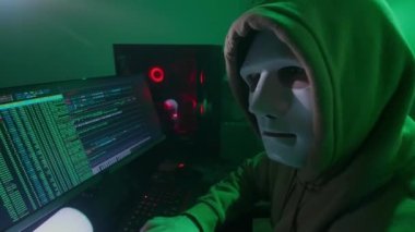 Beyaz maskeli anonim kişi bilgisayarda çalışıyor, kodları giriyor, klavyede çok hızlı yazıyor, bilgiyi kontrol ediyor, kodlama, çalışma, programlama, hackleme