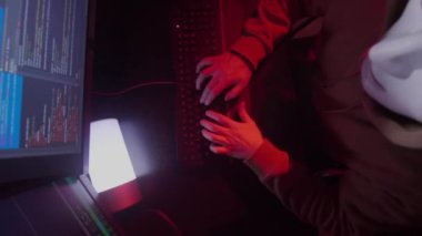 Beyaz maskeli anonim kişi bilgisayarda çalışıyor, kodları giriyor, klavyede çok hızlı yazıyor, fareye tıklıyor, bilgiyi kontrol ediyor, kodluyor, çalışıyor, programlıyor, hackliyor, oynuyor