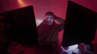 Beyaz bir adam beyaz bir maske takıyor, bilgisayarda çalışıyor, kodları giriyor, klavyeye çok hızlı giriyor, bilgiyi, kodlamayı, çalışmayı, programlamayı, hacklemeyi, oyunu kontrol ediyor.