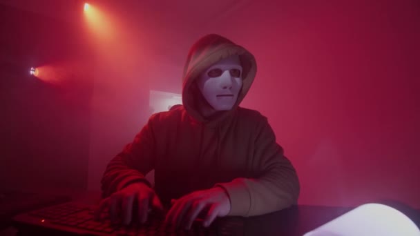 Anonyme Person mit weißer Maske arbeitet am Computer, gibt Code ein, tippt sehr schnell auf die Tastatur, überprüft die Informationen, kodiert, studiert, programmiert, hackt, spielt — Stockvideo