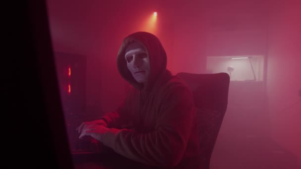 La persona anonima in una maschera bianca lavora sul computer, il codice di ingressi, i tipi molto veloci sulla tastiera, controlla le informazioni, la codifica, lo studio, la programmazione, l'hacking, il gioco — Video Stock