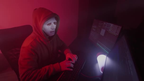 Personne anonyme dans un masque blanc travaille sur l'ordinateur, code d'entrée, types très rapide sur le clavier, vérifie les informations, codage, étude, programmation, piratage — Video