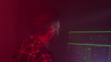 Gözlüklü beyaz bir adam bilgisayarda çalışıyor, kodları giriyor, klavyede çok hızlı yazıyor, bilgiyi kontrol ediyor, kodluyor, çalışıyor, programlıyor.