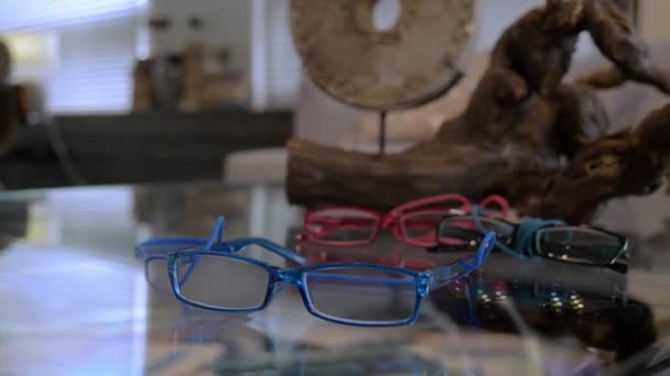 Een close-up van de blauwe bril die naast de rode bril en zwarte bril op tafel ligt — Stockvideo