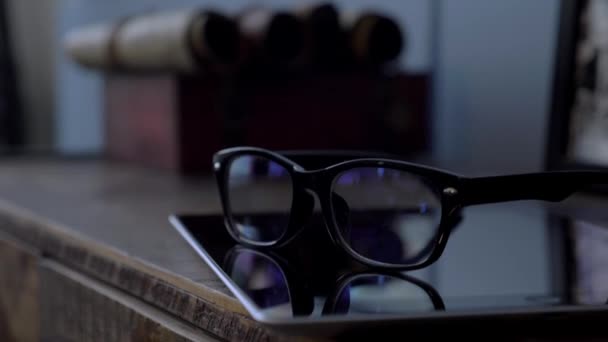 Gafas en borde negro acostado en una tableta en un tocador de madera en la habitación, de cerca — Vídeo de stock