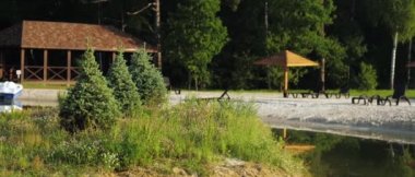 Beach area with sand and loungers near a small river in a cottage village in nature, rest near the water, sunny hot summer day, recreation area with summer houses and a dense soft-wood forest