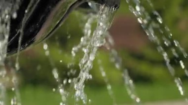 Close up on the water falling from the working fountain in the countryside in summer in a cottage village, park and recreation area on a hot day, freshness of water jets, reflections in drops