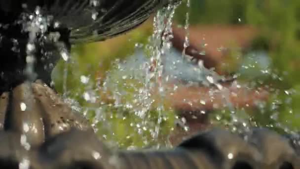 Close up on the splashing water falling from the working fountain in the countryside in summer in a cottage village, park and recreation area on a hot day, freshness of water, reflections in drops — Video Stock
