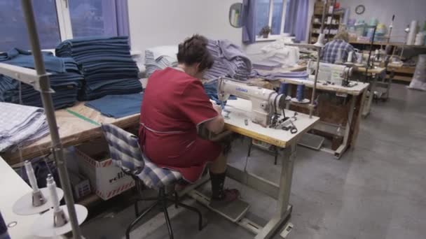 Tela producton trabajador en su lugar de trabajo, trabajando con una máquina de coser, haciendo ropa y telas — Vídeos de Stock