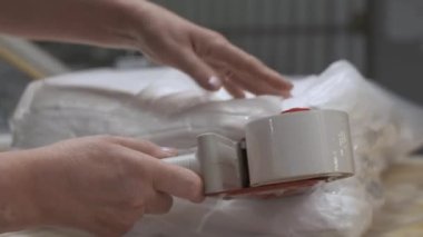 İşyerindeki tekstil işçisi, elleri kumaş ve kumaş fabrikasının bitmiş ürünlerini, nakliye için kumaş ambalajlarını paketliyor.