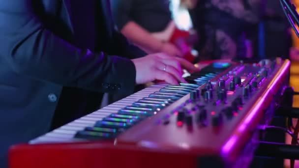 En kaukasisk man spelar elektriskt piano på en konsert, fest, musikfest, neonfärger, spelar ackord på tangenterna närbild, syntar, gör musik och improviserar på festen — Stockvideo