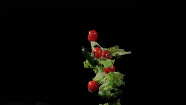 Mokra sałata, pomidory i ogórki latają i wirują z rozpryskami wody na czarnym tle w zwolnionym tempie strzał, krople wody na warzywa — Wideo stockowe