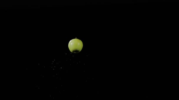 Frischer grüner Apfel fliegt auf und dreht sich mit Wasserspritzern auf schwarzem Grund in Zeitlupe, Wassertropfen auf Früchte
