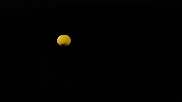 Nasse frische Zitrone fliegt auf und dreht sich mit Wasserspritzern auf schwarzem Hintergrund in Zeitlupe, Wassertropfen auf Früchte — Stockvideo