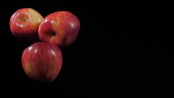 靠近一组三个新鲜的红苹果飞过来，在黑色的背景上缓慢地旋转着 — 图库视频影像