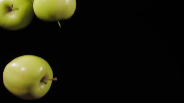 Avvicinati a un gruppo di tre mele verdi fresche che volano su uno sfondo nero al rallentatore — Video Stock