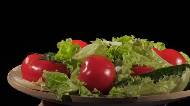 Tomates frescos, pepinos e alface são colocados em uma placa de madeira em um fundo preto, gotas de água em vegetais. — Vídeo de Stock