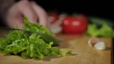 Erkeklerin ellerine yaklaş. Siyah arka planda tahtayı keserken bıçakla marul kes.