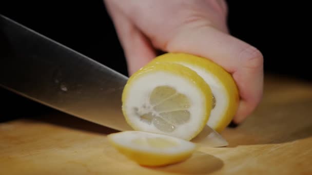 Close up op mens handen gesneden citroen met een mes in stukken op snijplank op een zwarte achtergrond — Stockvideo