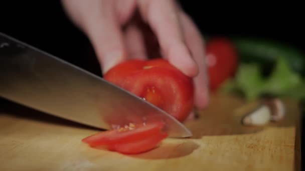 Close-up em homens mãos cortar tomate com uma faca em pedaços na placa de corte em um fundo preto — Vídeo de Stock