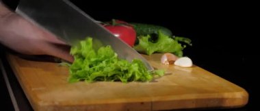 Erkekler, siyah arka planda tahtayı keserken bıçakla taze marul keserler.