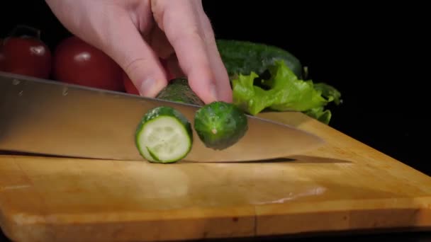 Erkekler siyah arka planda tahtayı keserken bıçakla salatalık keserler. — Stok video